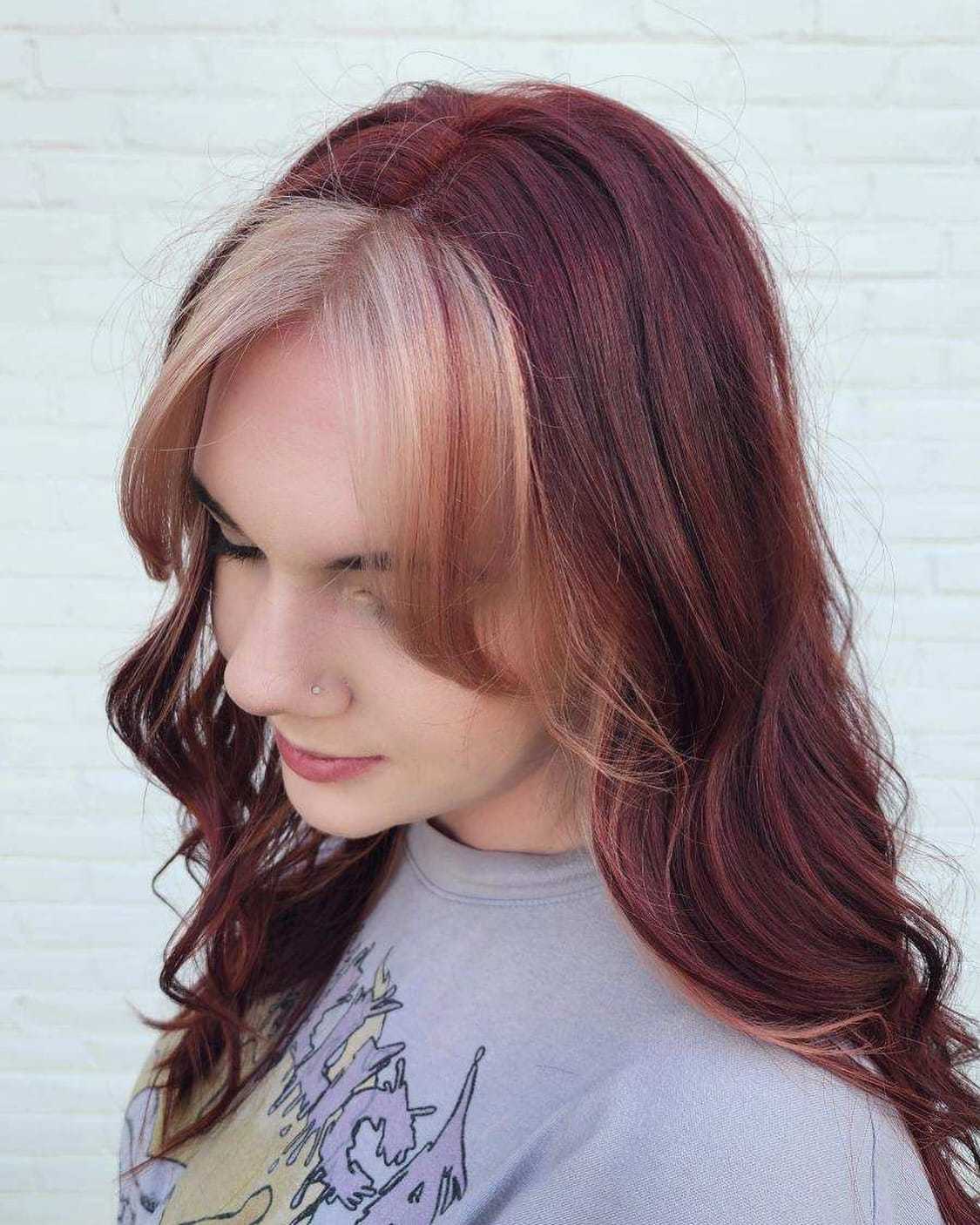 Woman with red hair and blonde highlights wearing a grey shirt, looking down indoors.
