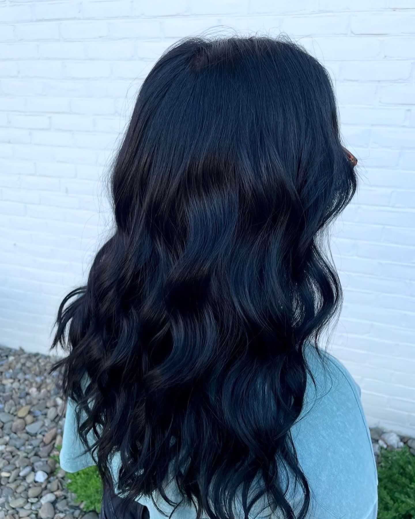 Person with long, wavy black hair standing against a white brick wall.